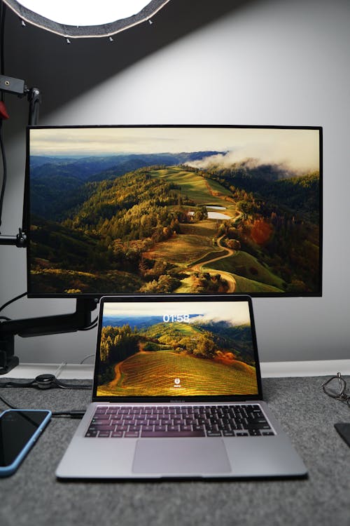 A laptop and monitor on a desk with a mountain view
