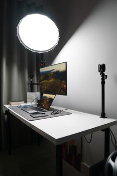 A minimalist desk setup with a laptop, monitor, and studio lamp, reflecting contemporary workspace design.