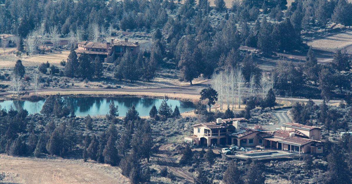 A scenic aerial view of rustic houses surrounded by trees and a pond, evoking a tranquil, natural atmosphere.