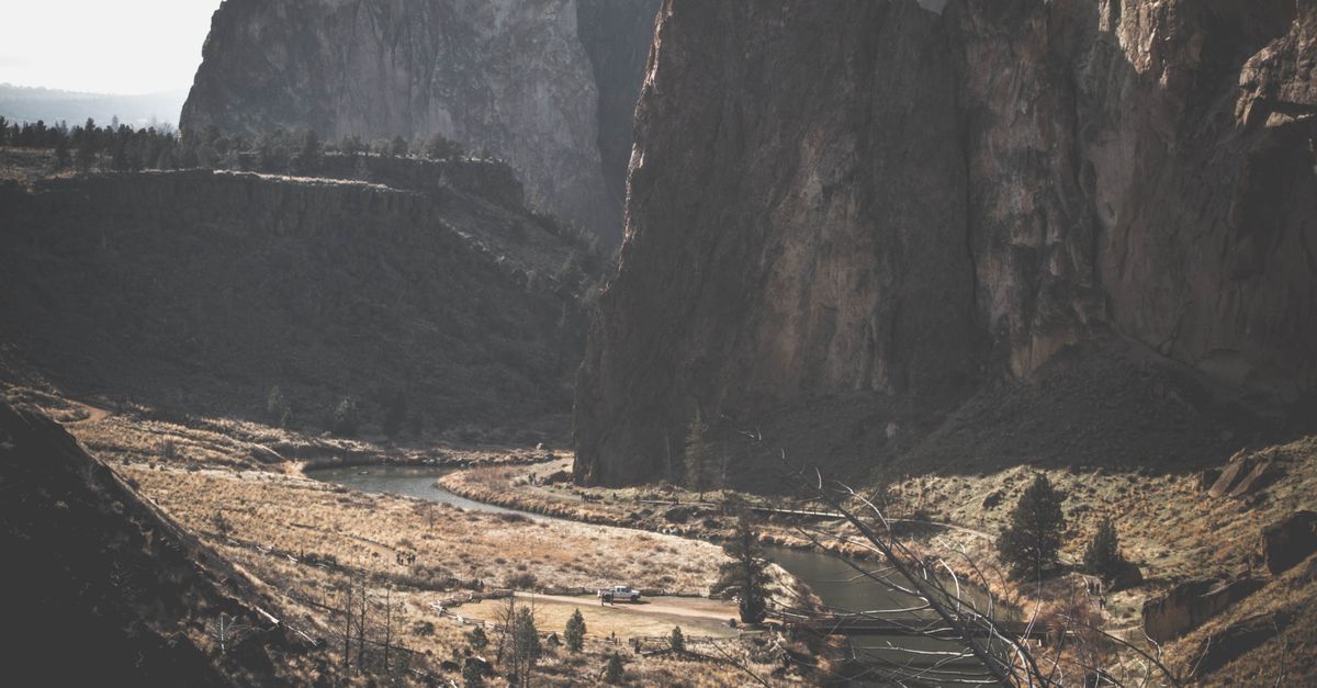 A breathtaking landscape of a river winding through a valley with towering cliffs and rugged terrain under daylight.