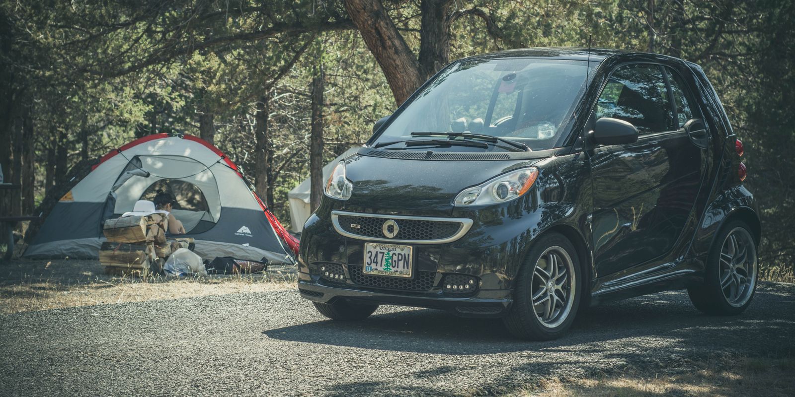 A tent pitched at a wooded campsite beside a car