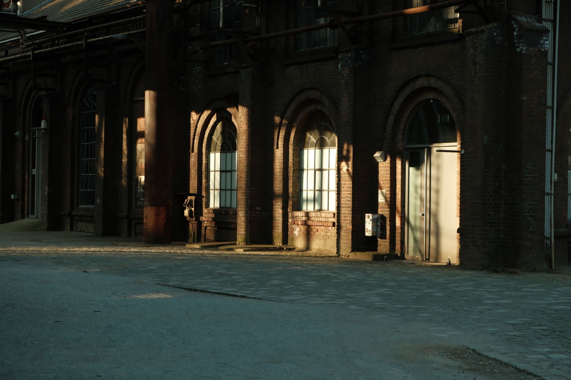 A vintage industrial building exterior with arched windows and shadows at sunset.