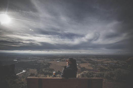 Person enjoys serene landscape view from a bench under cloudy sky.