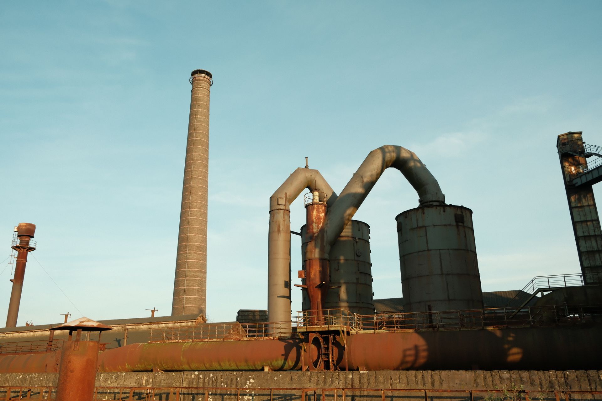 An abandoned and rusty factory with towering chimneys under a clear sky.