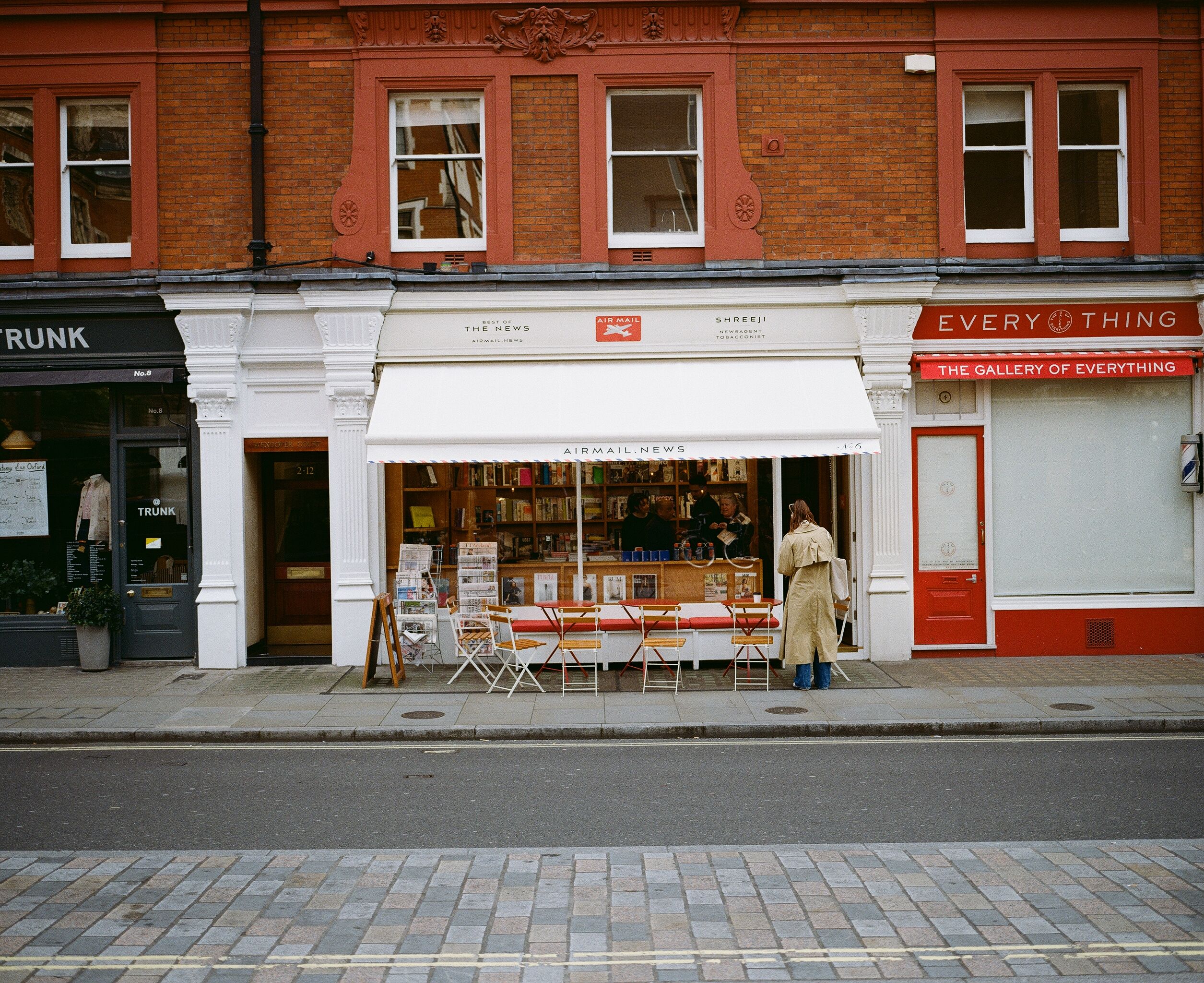 A quaint newsstand with red brick exterior and sidewalk seating in a busy urban area.