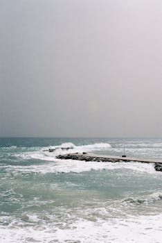 A stormy ocean scene with waves crashing against a rocky pier.