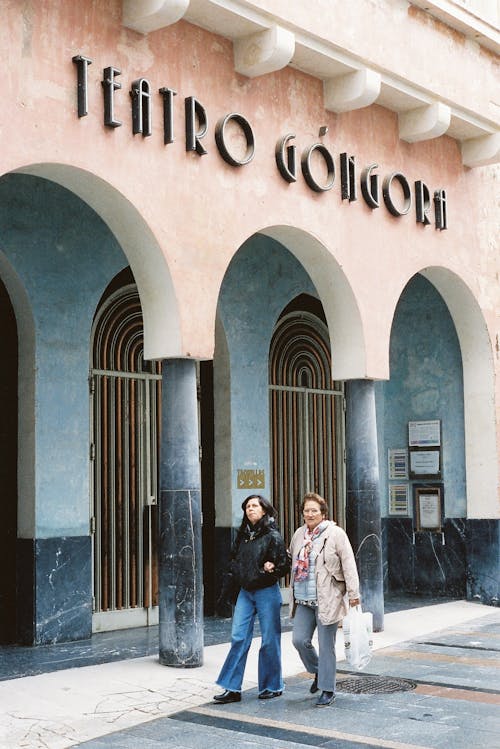 Free Two women standing outside of a building with the word edoqui Stock Photo