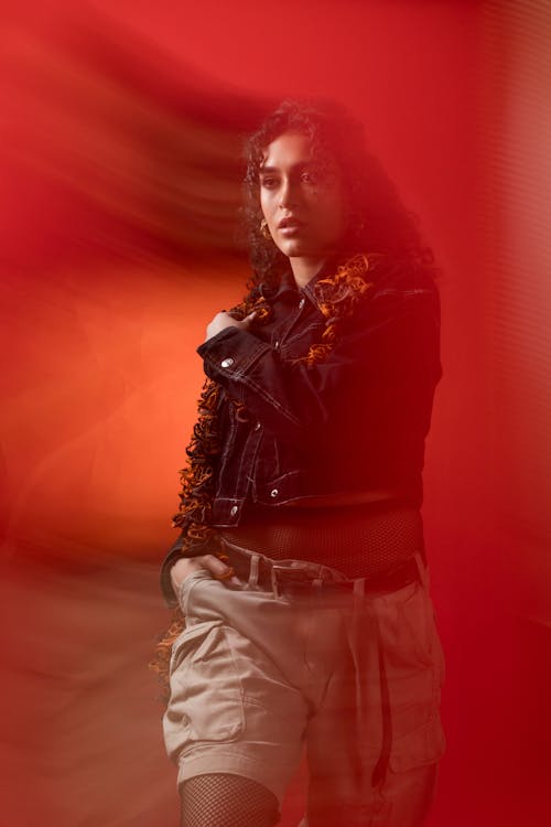 Free A woman in shorts and a jacket standing in front of a red background Stock Photo