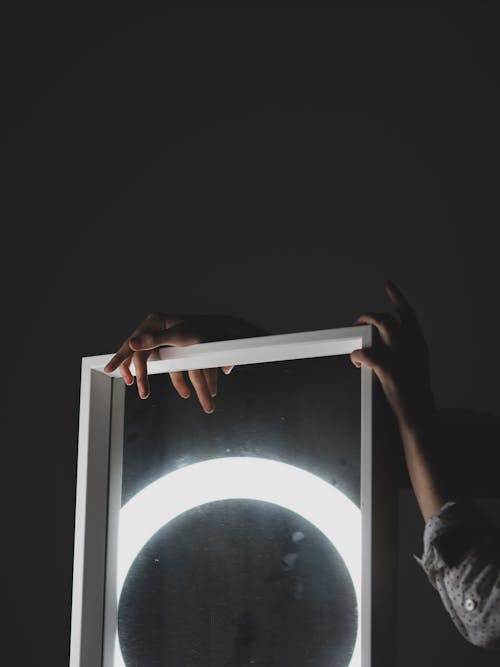 A person holding a lighted mirror with a moon in the background