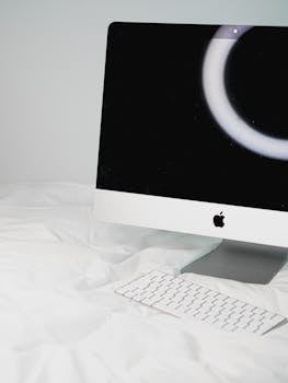 A sleek desktop computer setup on a comfortable white bed with a futuristic screensaver.