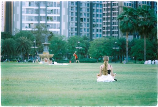A woman in a park meditates, offering a serene contrast against a bustling cityscape.