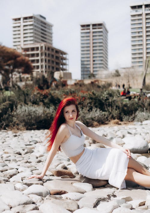 A woman with red hair sitting on rocks in front of buildings
