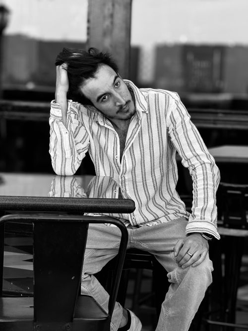 Free A relaxed man sitting at a table, styling his hair with a casual pose. Stock Photo