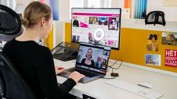A woman conducts a professional video call while working at her desk in a bright office setting.