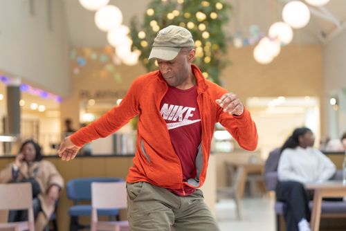 Free A man in an orange jacket dances energetically in a brightly lit café, capturing motion and joy. Stock Photo