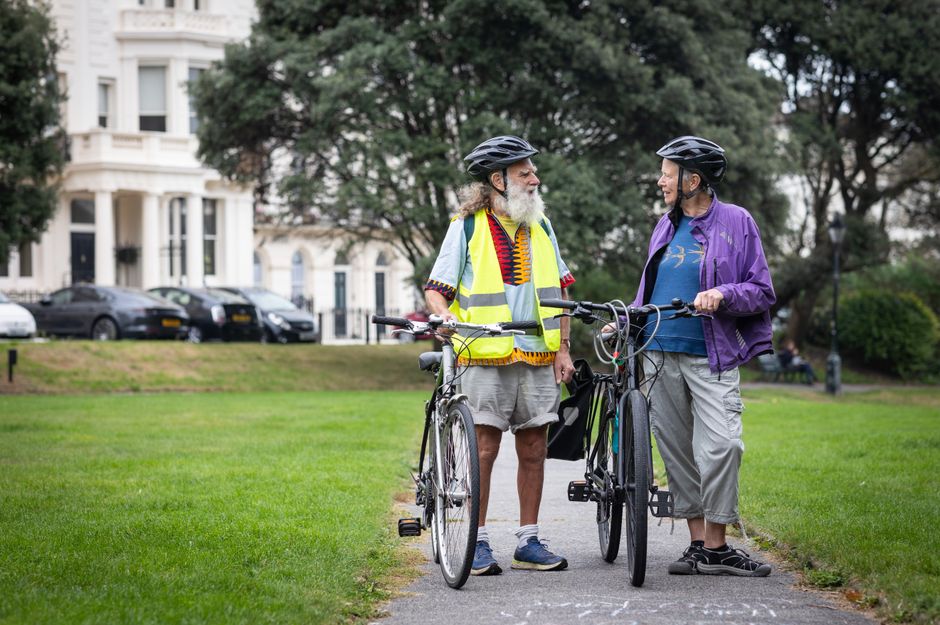 Two senior men with bicycles and helmets, enjoying a talk in a scenic outdoor park.