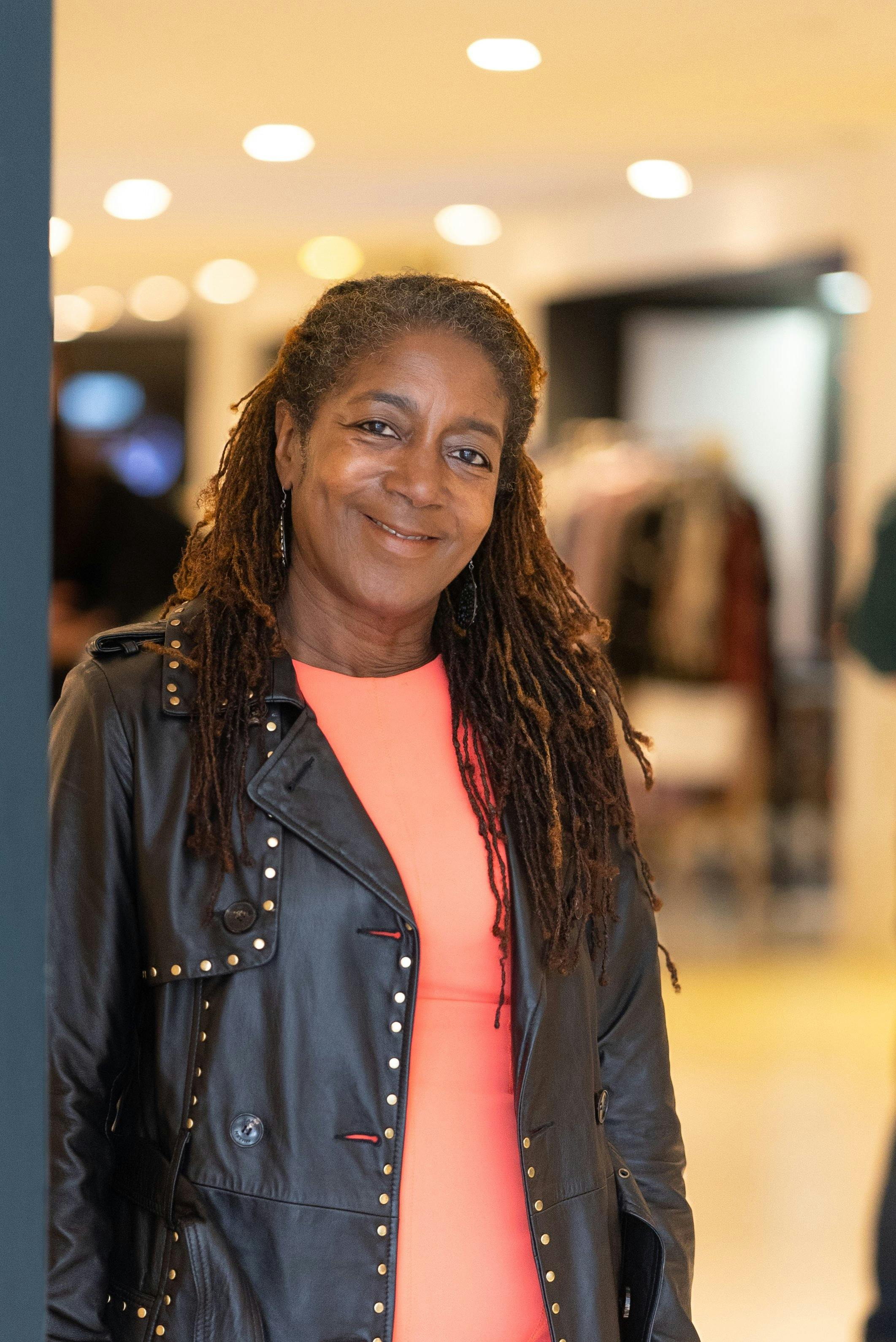 Portrait of a confident woman with dreadlocks in a studded leather jacket and pink blouse.
