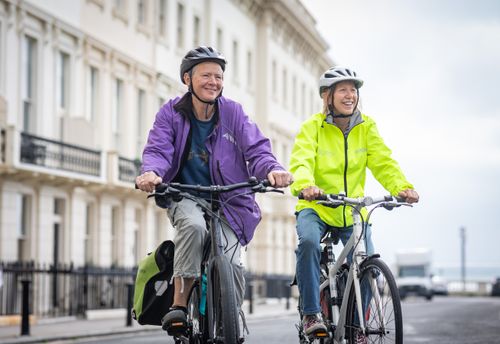 Free Smiling senior adults riding bicycles in a city street, enjoying urban cycling. Stock Photo