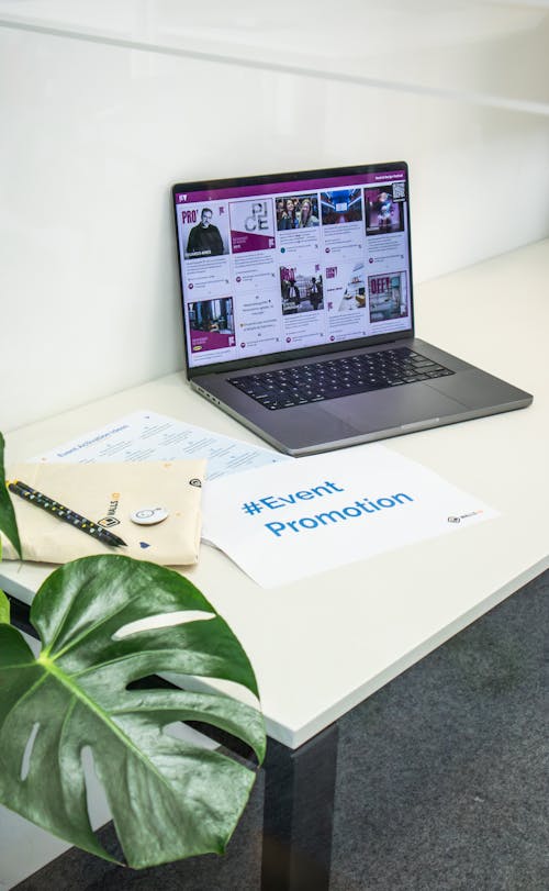A collection of branded merch and freebies for events with the hashtag #EventPromotion and a laptop showing a social media wall