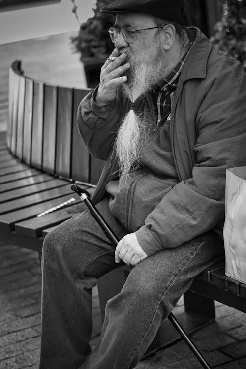 Free An old man sitting on a bench smoking a cigarette Stock Photo