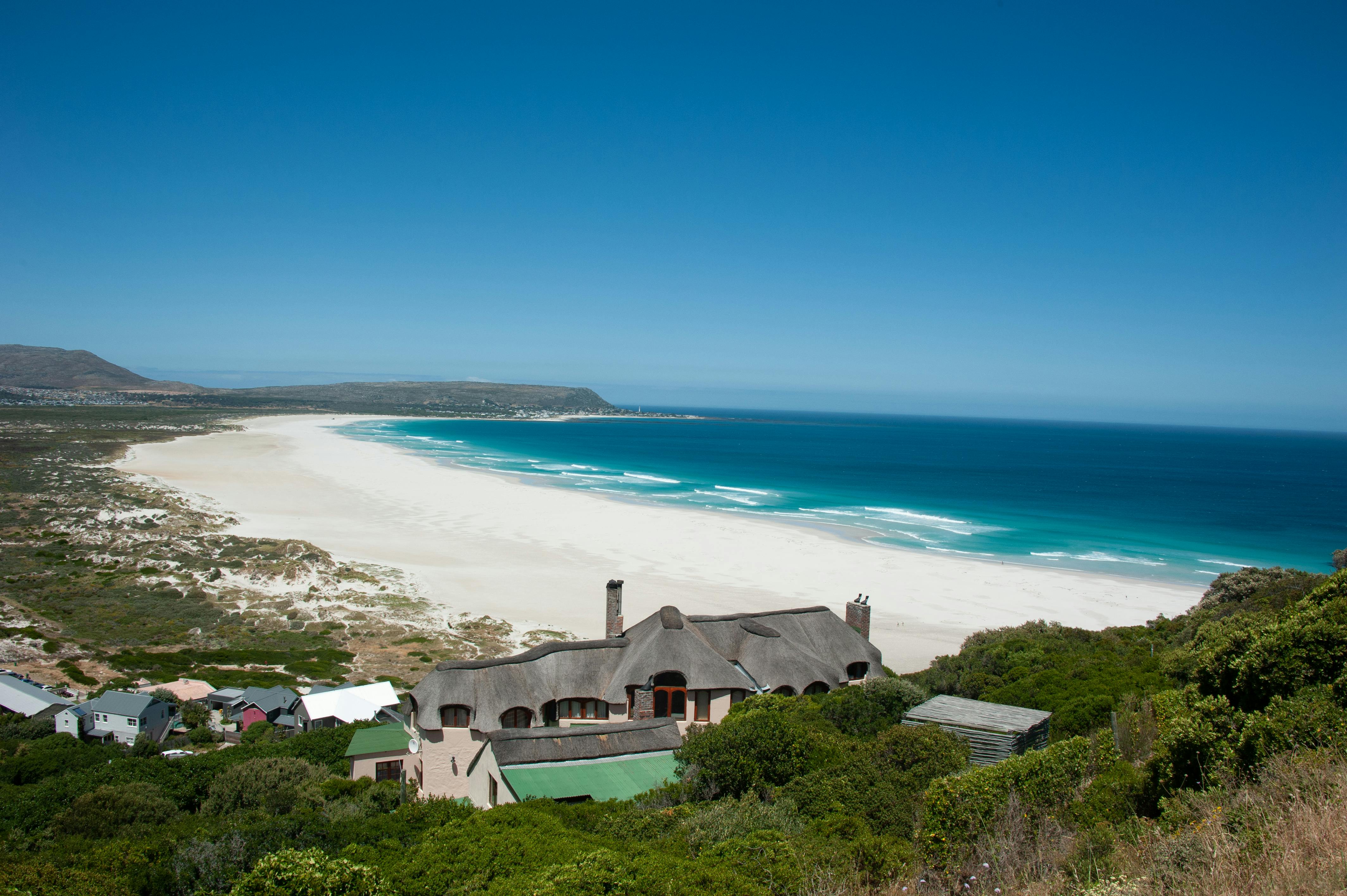 从令人惊叹的鸟瞰视角俯瞰，宁静的海岸线旁，房屋点缀，清澈的蓝色海洋在明亮的天空下延伸