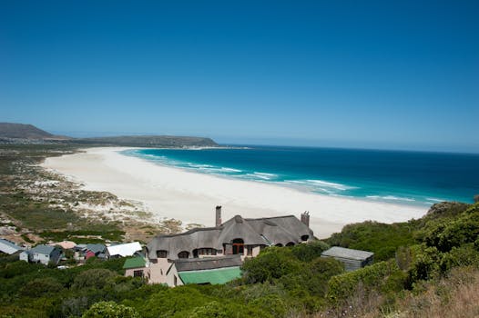 从令人惊叹的鸟瞰视角俯瞰，宁静的海岸线旁，房屋点缀，清澈的蓝色海洋在明亮的天空下延伸