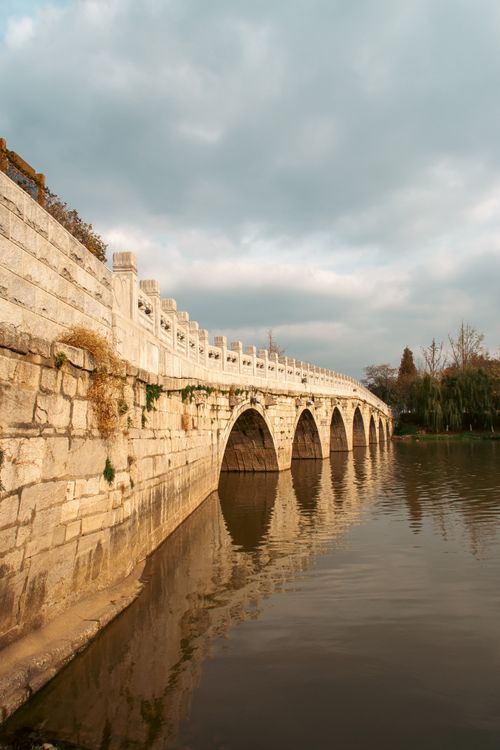 Free Ancient stone bridge reflection on a peaceful river under a cloudy sky in Nanjing, China. Stock Photo