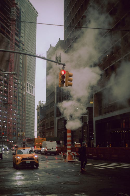 A city street with a yellow taxi and smoke coming out of a building