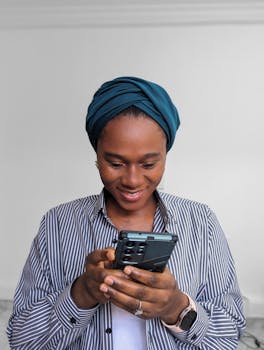 A woman in headwear smiles while using her smartphone against a white background.