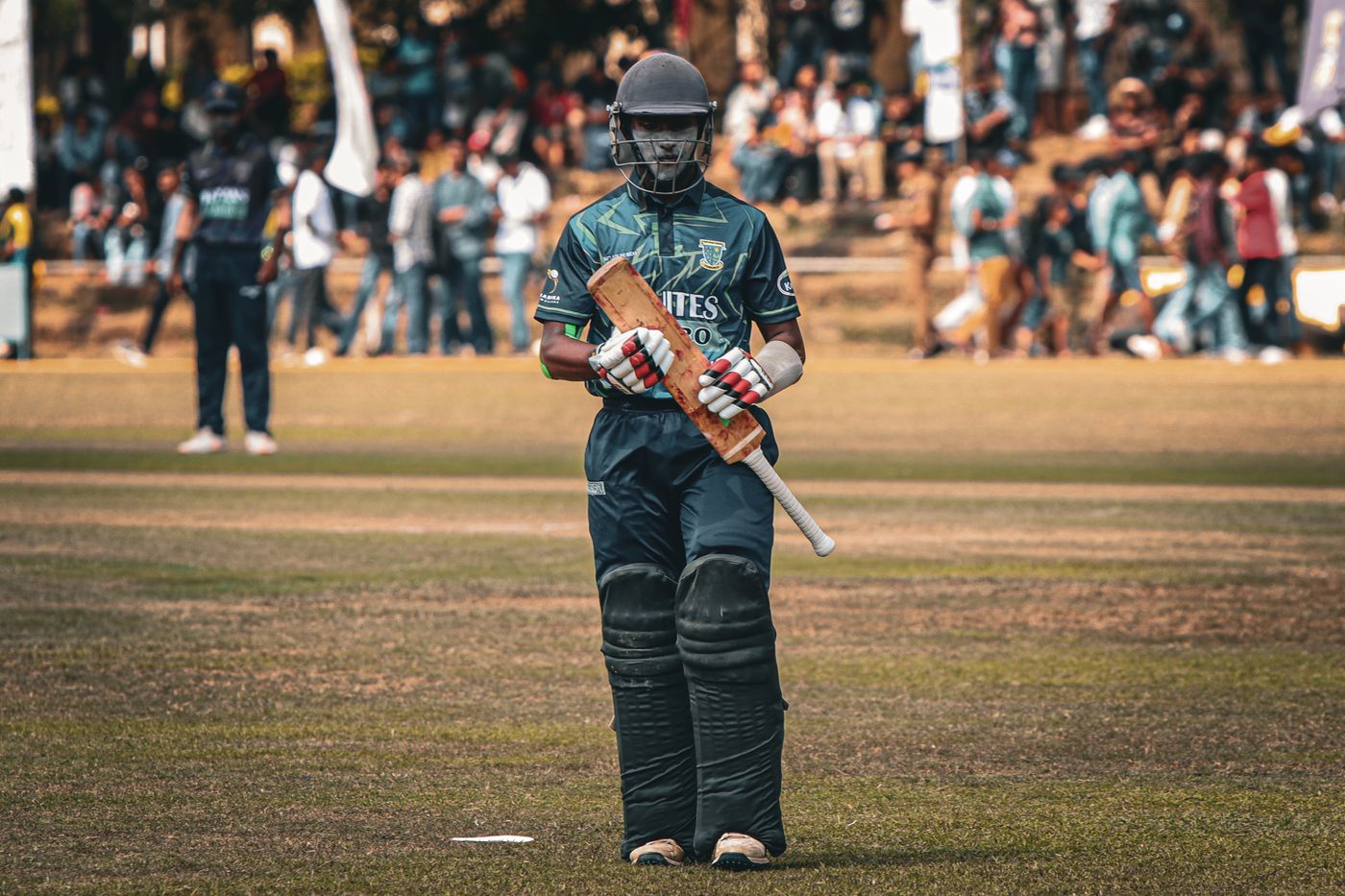 Cricket player walking on the field with bat