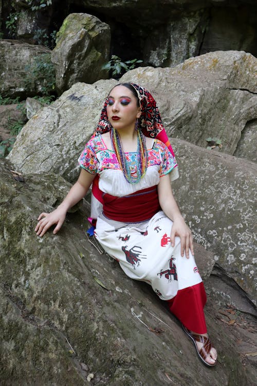 Free Model in Embroidered Blouse and Headscarf Sitting on a Rock Stock Photo