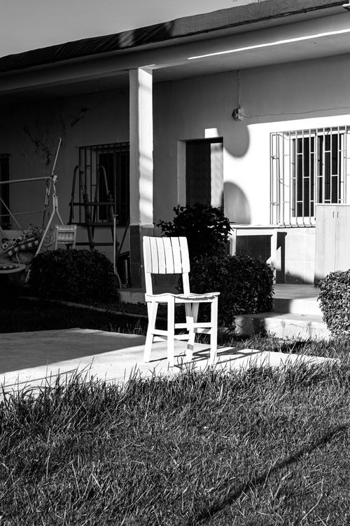 Free Black and white photo of a residential building with a lone chair on the porch. Stock Photo