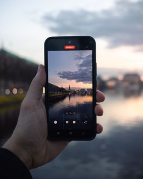 A hand holding a smartphone capturing the serene sunset view of Hamburg's skyline.
