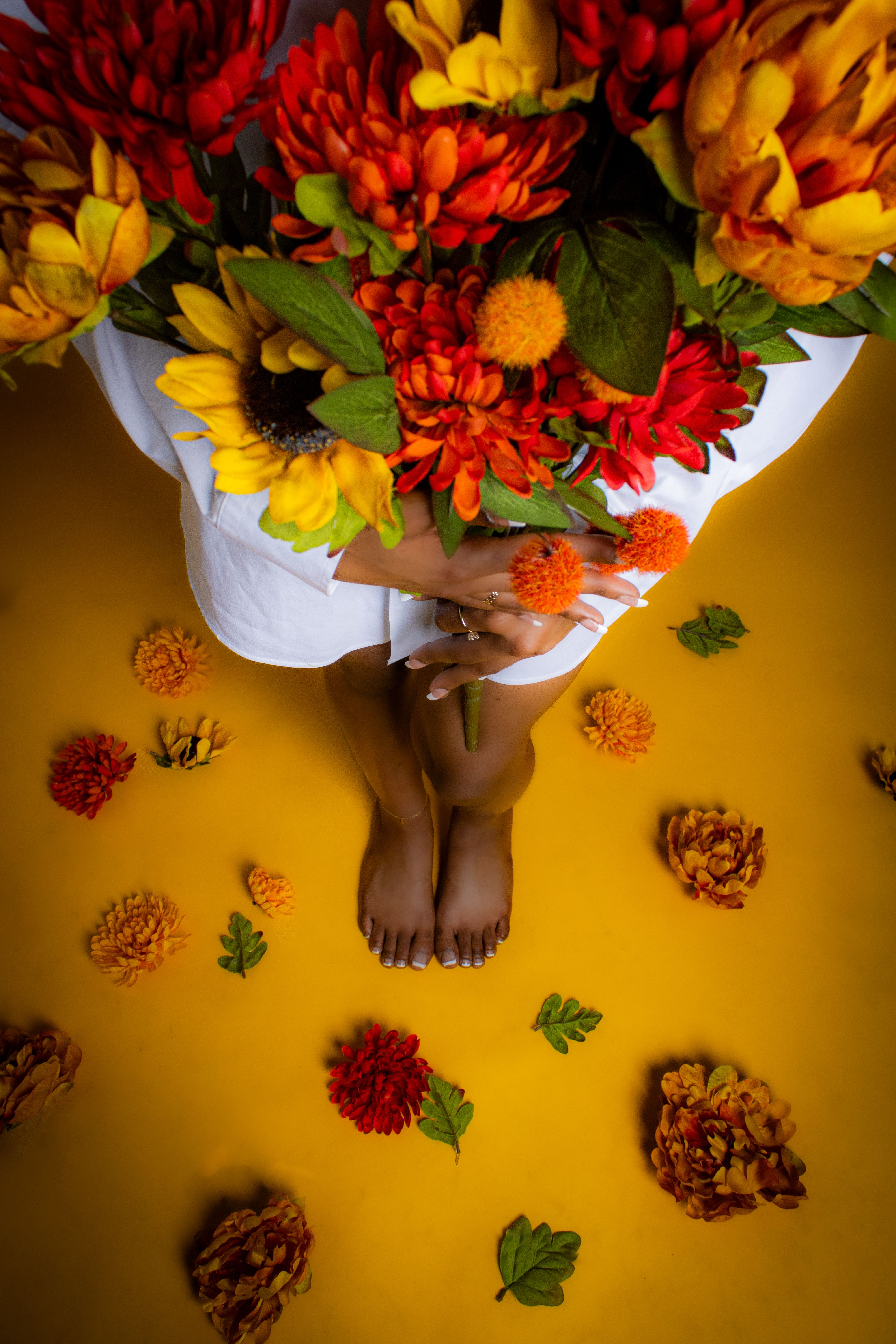 A close-up shot of a vibrant floral bouquet held by an adult woman, surrounded by scattered flowers on a yellow background.