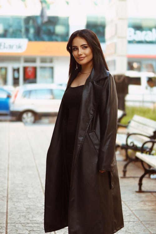 Free A woman in a black coat and dress standing on a sidewalk Stock Photo