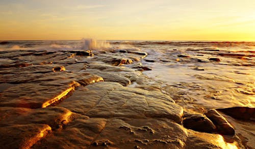 View of Waves Crashing on a Rocky Shore at Sunset 