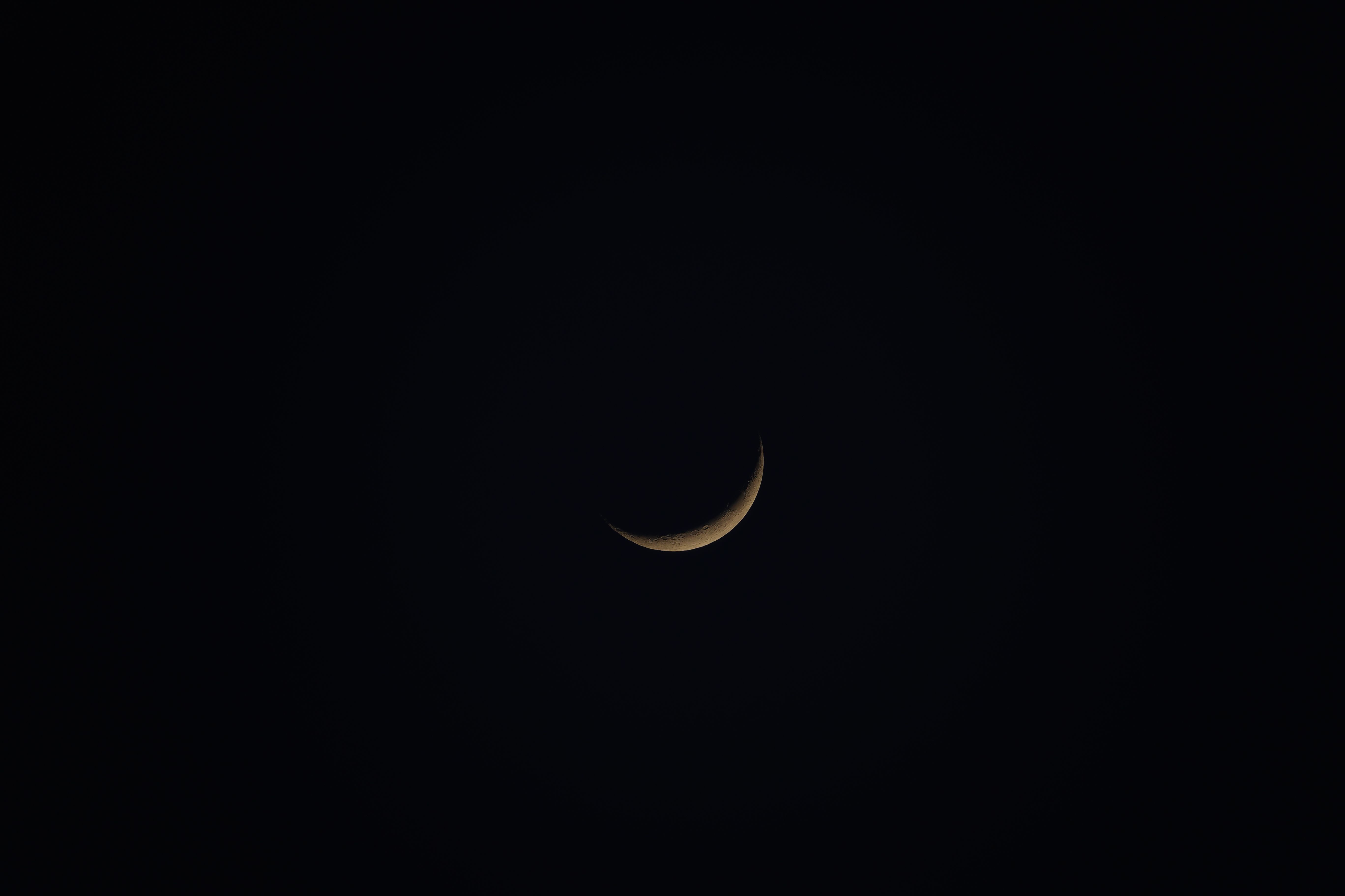 A thin crescent moon glowing alone in a dark night sky, like the first sliver that appears after a new moon