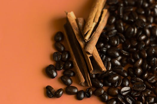 Aromatic cinnamon sticks and coffee beans artfully arranged on a warm orange background.