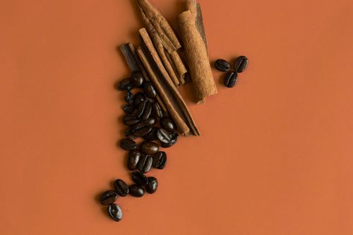 Free Flat lay of cinnamon sticks and coffee beans on an orange background, perfect for food and spice themes. Stock Photo