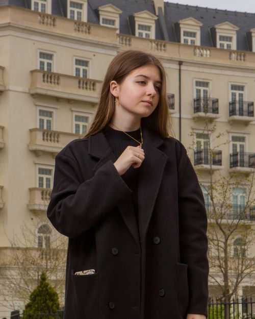 Free Portrait of a fashionable woman in a black coat posing outdoors by a classic building. Stock Photo