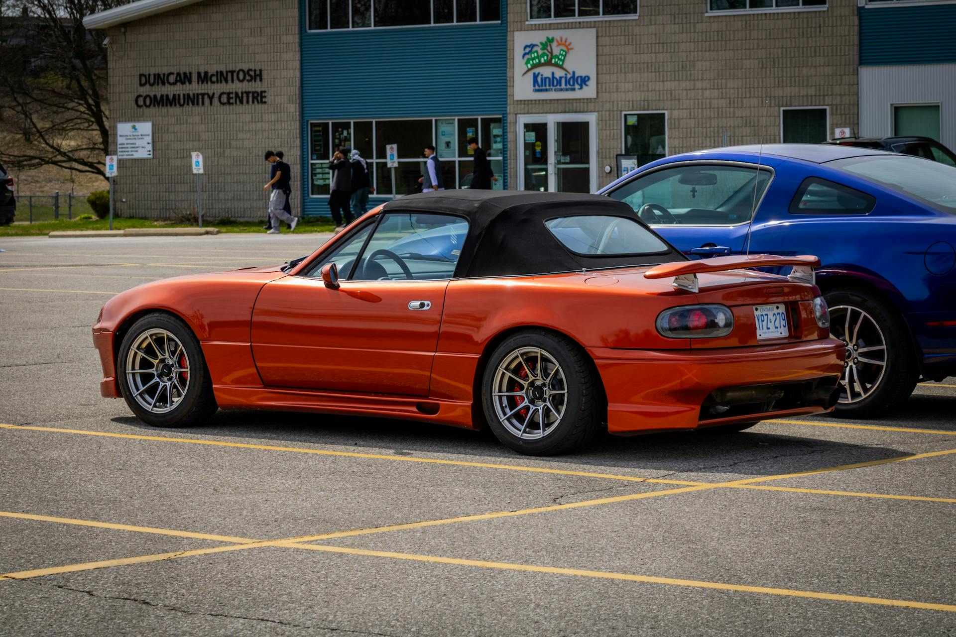 Tuned red convertible sports car parked in an urban lot in front of a community center.