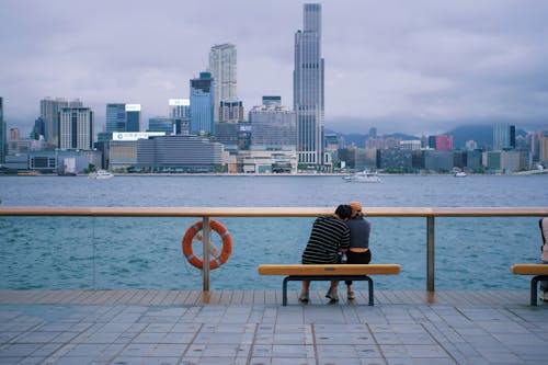 Free Two people sitting on a bench overlooking a city Stock Photo