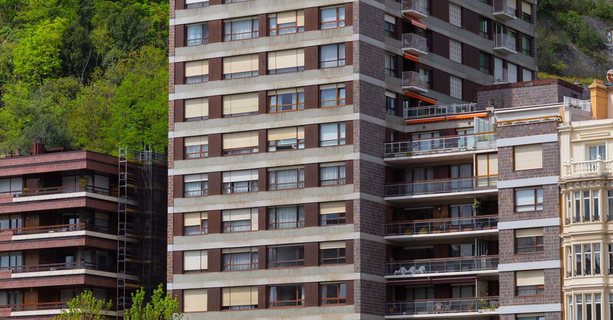 Edifícios altos ao lado do rio Nervión em Bilbau, com vegetação exuberante, simbolizando estruturas residenciais protegidas por seguro contra intempéries
