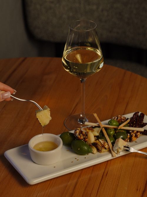 Free Savor an elegant cheese platter with nuts, olives, and a glass of white wine in a cozy setting. Stock Photo