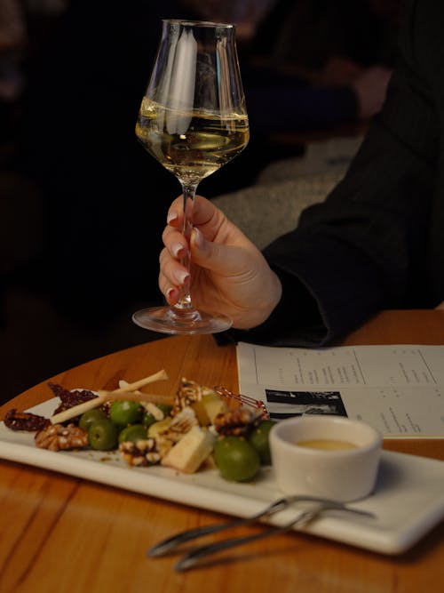 Free A person holding a glass of wine over a plate of food Stock Photo