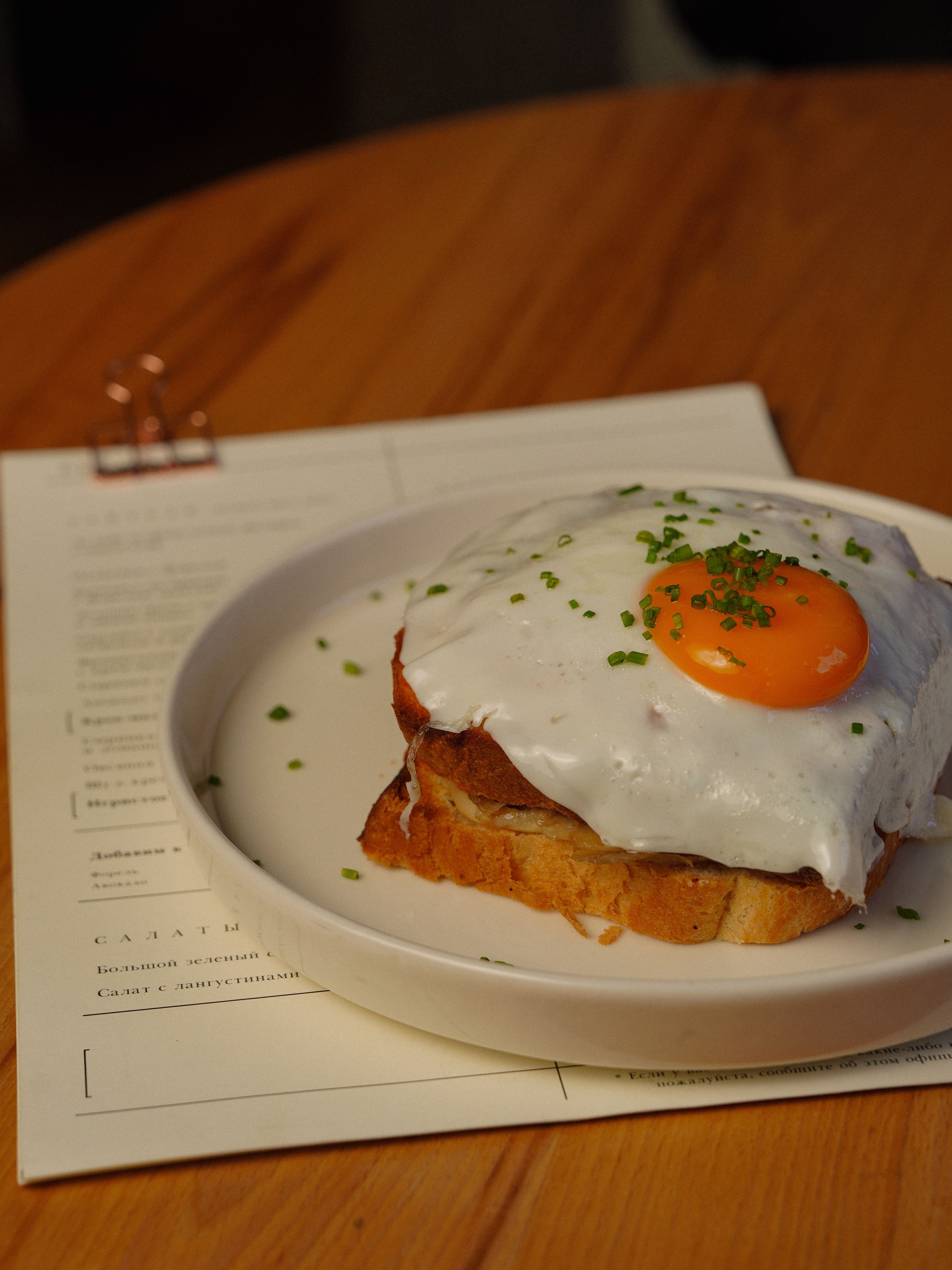 A croque madame on a plate, ham and melted Gruyère between grilled bread, topped with a fried egg with a runny yolk, béchamel sauce visible at the edges.