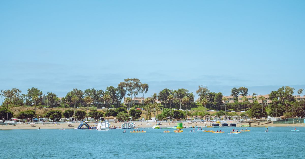 Kayaks and people enjoying the summer at Newport Beach, CA, with a clear blue sky and calm sea.