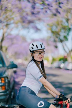 A woman in sportswear cycling on a tree-lined street with purple flowers. Outdoor recreation and fitness.