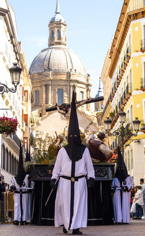 Free A religious Easter procession in Zaragoza with hooded participants and a historic dome background. Stock Photo