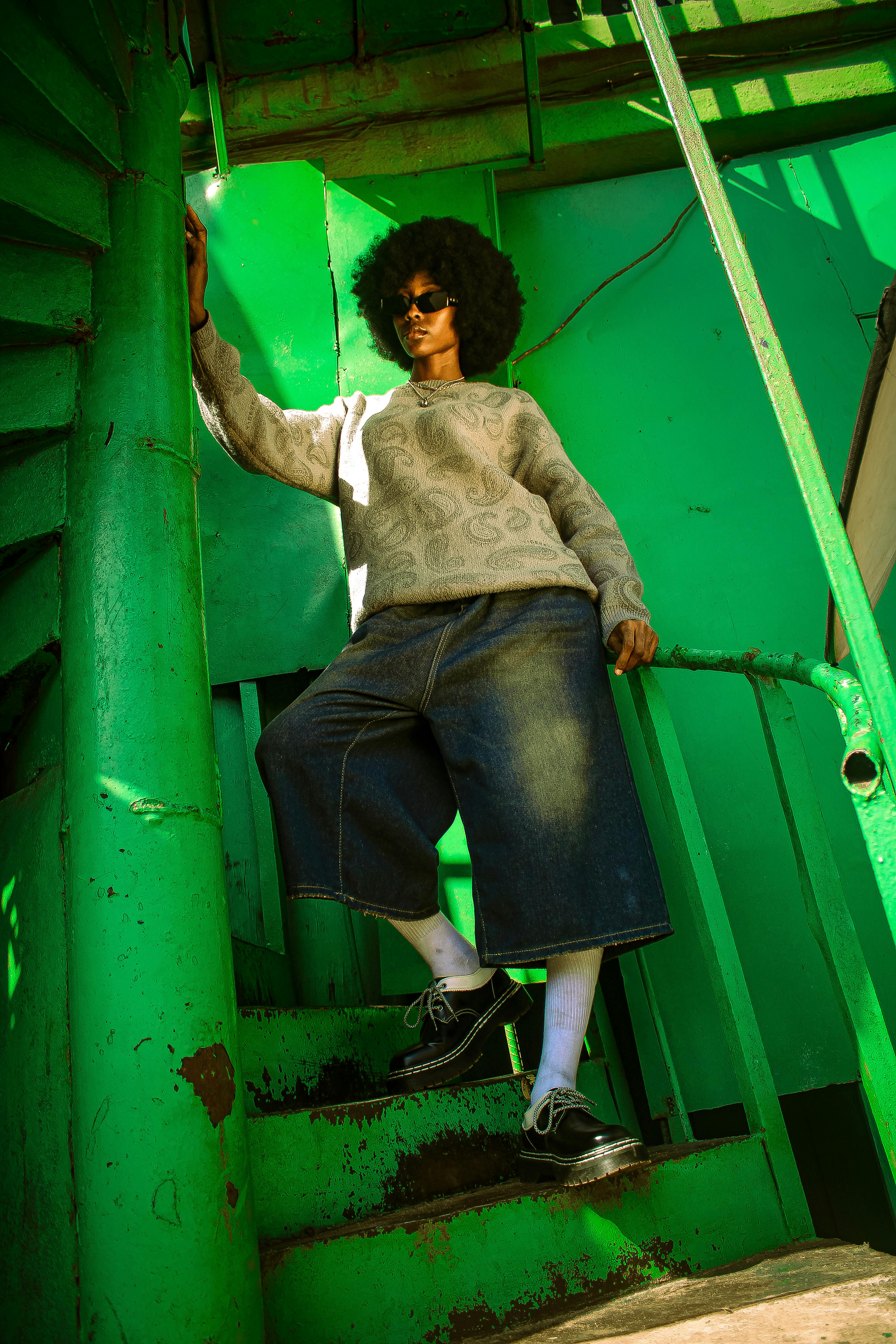 Stylish person in streetwear poses on green stairs, highlighting modern urban fashion.